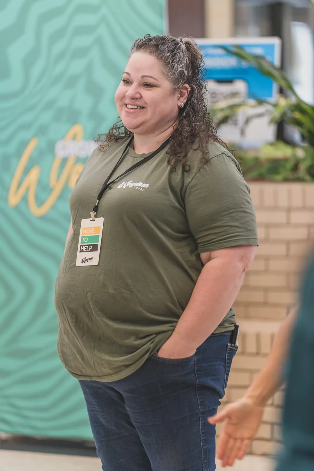 A Kingdom House volunteer in a Here To Help badge greeting guests outside