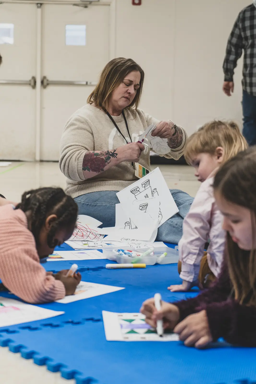 A Kingdom Kids volunteer coloring with children on the classroom floor
